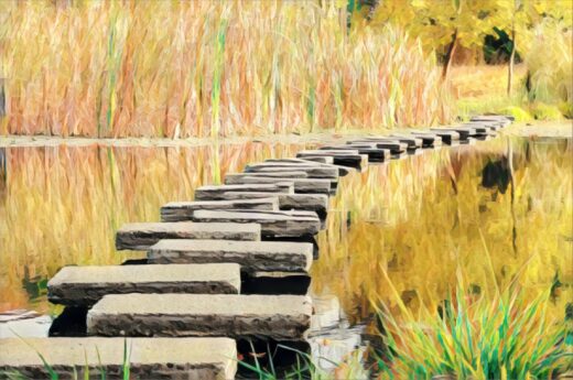 Steinweg über ruhiges Wasser im Herbst mit goldenen Schilfrohren und buntem Laub.