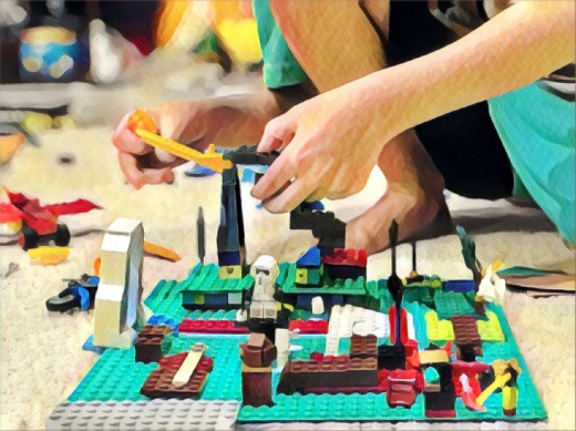 Kinderhände bauen fantasievolles LEGO-Modell auf grünem Teppichboden. Bunte Steine verstreut.